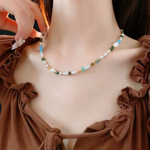 Elegant pearl necklace with gold, green, and blue beads on a fashion model neckline