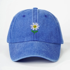 Close-up of white daisy embroidery with a yellow smiley face on blue denim baseball cap