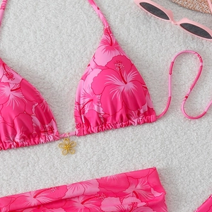 Detailed view of pink floral bikini top with a gold flower charm on a textured background