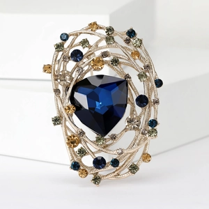 Detailed view of a golden nest brooch featuring a large blue gem and colored rhinestones