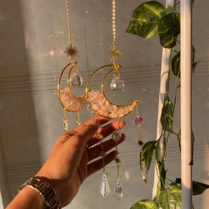 Detail of two gold moon suncatchers with natural pink crystal stones and faceted pendants