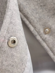 Detailopname van de lichtgrijze wollen stoftextuur en de metalen drukknoppen van de jas