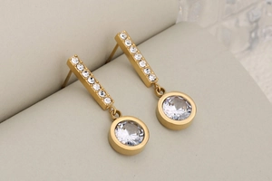 Detail of gold drop earrings featuring a long bar and round pendant with white zircons