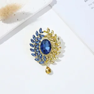 Elegant gold wreath brooch with deep blue oval gemstone and yellow teardrop pendant