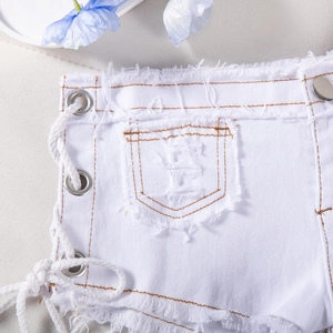 Dettaglio di pantaloncini in denim bianco con frange e allacciatura laterale con occhielli