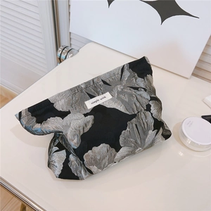 Detail of black floral jacquard makeup bag with simple wish label on white vanity