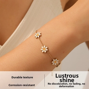 Close-up of elegant gold chain bracelet with three white enamel daisy charms on wrist