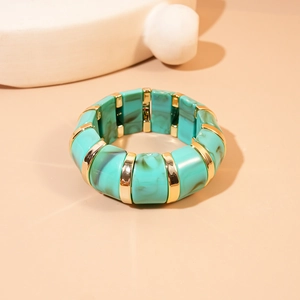 Detail of turquoise marble resin bangle with gold-tone metal segments on a beige surface