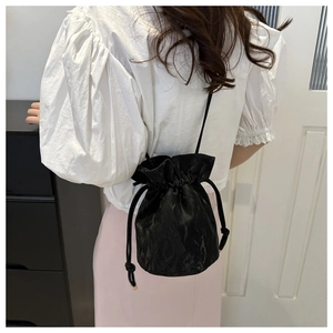 Detail shot of black drawstring bucket bag featuring pleated texture and slender strap