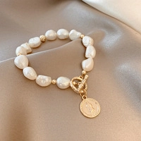 Pulsera de perlas barrocas con colgante de moneda de oro y cierre OT sobre raso crema