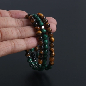 Hand holding malachite and tiger eye natural stone beaded bracelet with metal spacers