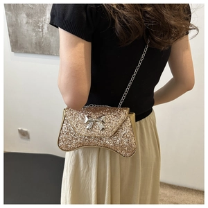 Model wearing a gold glitter evening bag with metal chain strap and bow detail