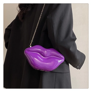 Detail of a shiny purple lip-shaped box bag with gold chain strap on a black blazer