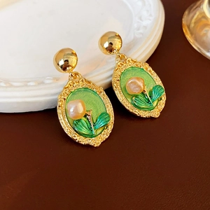 Macro shot of vintage gold earrings with green enamel floral accents and pearl details