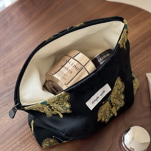 Elegant Chinese style black jacquard makeup bag with gold butterfly embroidery on a table