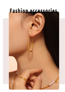 Close-up of golden paperclip earrings with minimalist gold ring and pearl necklace