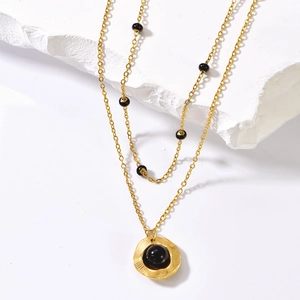 Detail of a double-layer gold necklace featuring a black pearl on a concave gold disc