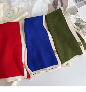Close-up of knitted scarves in red, blue, and olive green with beige trim on a table
