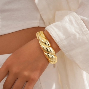 Close-up of golden chunky twisted rope bangle on female wrist with white linen shirt