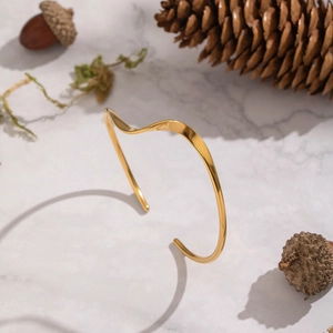 Minimalist gold stainless steel wave cuff bracelet on marble with natural elements