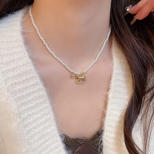 Close-up of pearl necklace with gold rocking horse pendant and crystal accents on neck