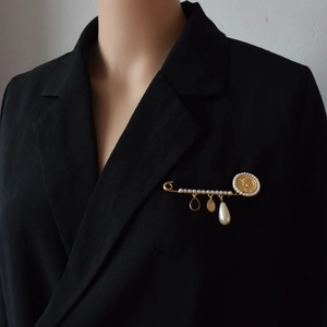 Baroque pearl brooch with coin and tassel pendants on a black blazer lapel