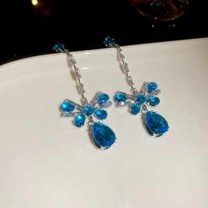 Detailed view of silver bow earrings with blue teardrop zircon and sparkling gemstones