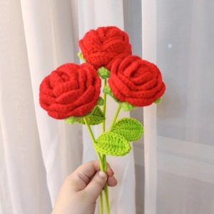 Handmade crochet red roses bouquet with green leaves held against soft white light