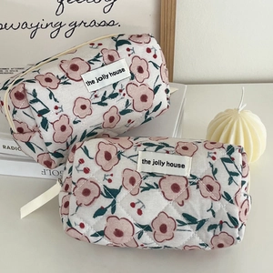 Detail van een gewatteerde toilettas met bloemenprint op een witte kaptafel met decoratie