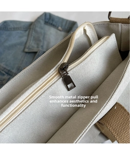 Detail of metal zipper closure on canvas tote bag with woven brown handle