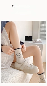 Détail de chaussette en coton crème avec bord ondulé, broderie planète et chaussures