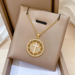 Detail of gold necklace featuring round cross pendant with white pearl and sparkling zircons
