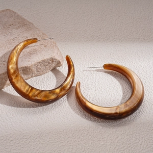 Close-up of amber resin C-shaped earrings with marble texture on light stone surface