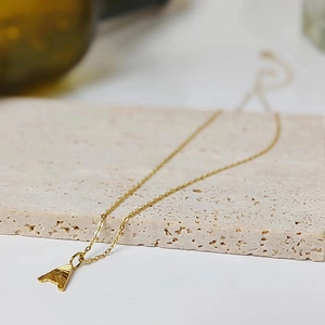Macro detail of gold letter A pendant with sunburst texture on a minimalist fine chain
