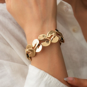 Close-up of a wide gold metal S-shaped twisted chain bracelet worn on a model's wrist