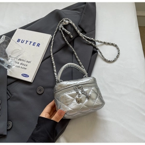 Detail of silver quilted mini bag with heart zipper pull and chain strap on white fabric