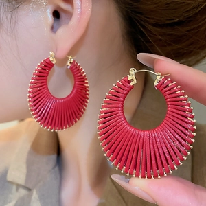 Détail de boucles d'oreilles créoles tressées en cuir rouge avec bordure dorée