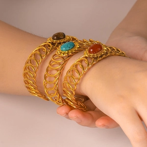 Three-piece gold spiral bracelets set with oval stones in brown, blue and red on wrist