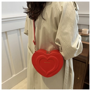 Red heart-shaped crossbody bag with gold hardware worn over a beige trench coat