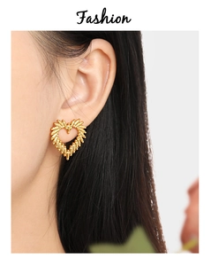 Detailed view of hollow gold heart earrings with unique grain texture on a female model