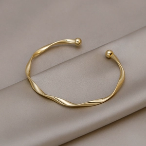 Elegante bracciale rigido dorato a torsione con sfere su lussuoso tessuto di seta