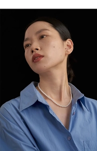 Detail view of vintage pearl necklace worn by a model in a light blue shirt