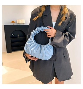 Detail of blue pleated crescent bag in high-quality faux leather held by a model