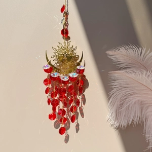 Close-up of golden sun and moon suncatcher with red crystal beads casting shadows