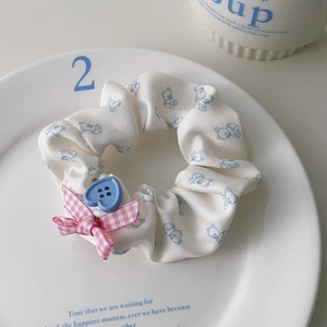 Détail d'un chouchou blanc motif ours avec nœud rose et bouton cœur bleu sur une assiette