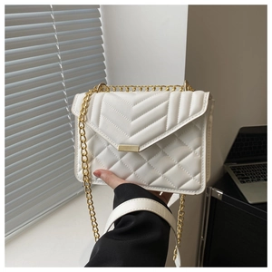 Detail of white quilted chain bag with gold hardware held in hand for scale