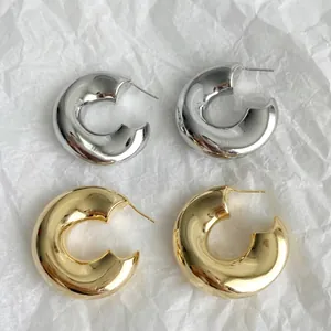 Detail van dikke C-vormige oorringen in gepolijste goud- en zilverkleurige metalen