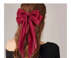 Detail view of a large burgundy satin bow hair clip with long ribbons on wavy hair