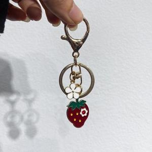 Detailed close-up of golden lobster clasp with red strawberry and small white flower charms