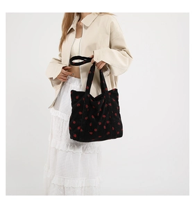 Close-up of black corduroy tote bag with red strawberry pattern and long shoulder straps